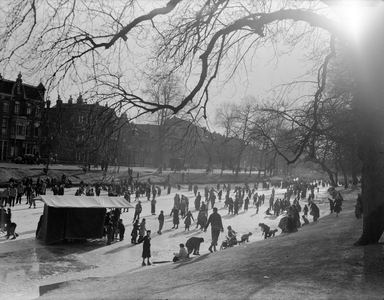 821072 Afbeelding van schaatsende mensen op de bevroren Stadsbuitengracht te Utrecht, ter hoogte van het Manenburg, met ...